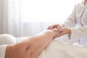 Elderly patient in bed with doctor’s hand, questioning whether bedsores are always a sign of nursing home neglect.