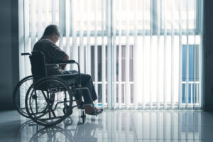 A man in a wheelchair looks out a window and wonders what the lowest-rated nursing homes in Savannah are.