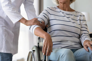 A caregiver helping an older woman in a nursing facility, illustrating the standard of care involved in preventing nursing home mistreatment.